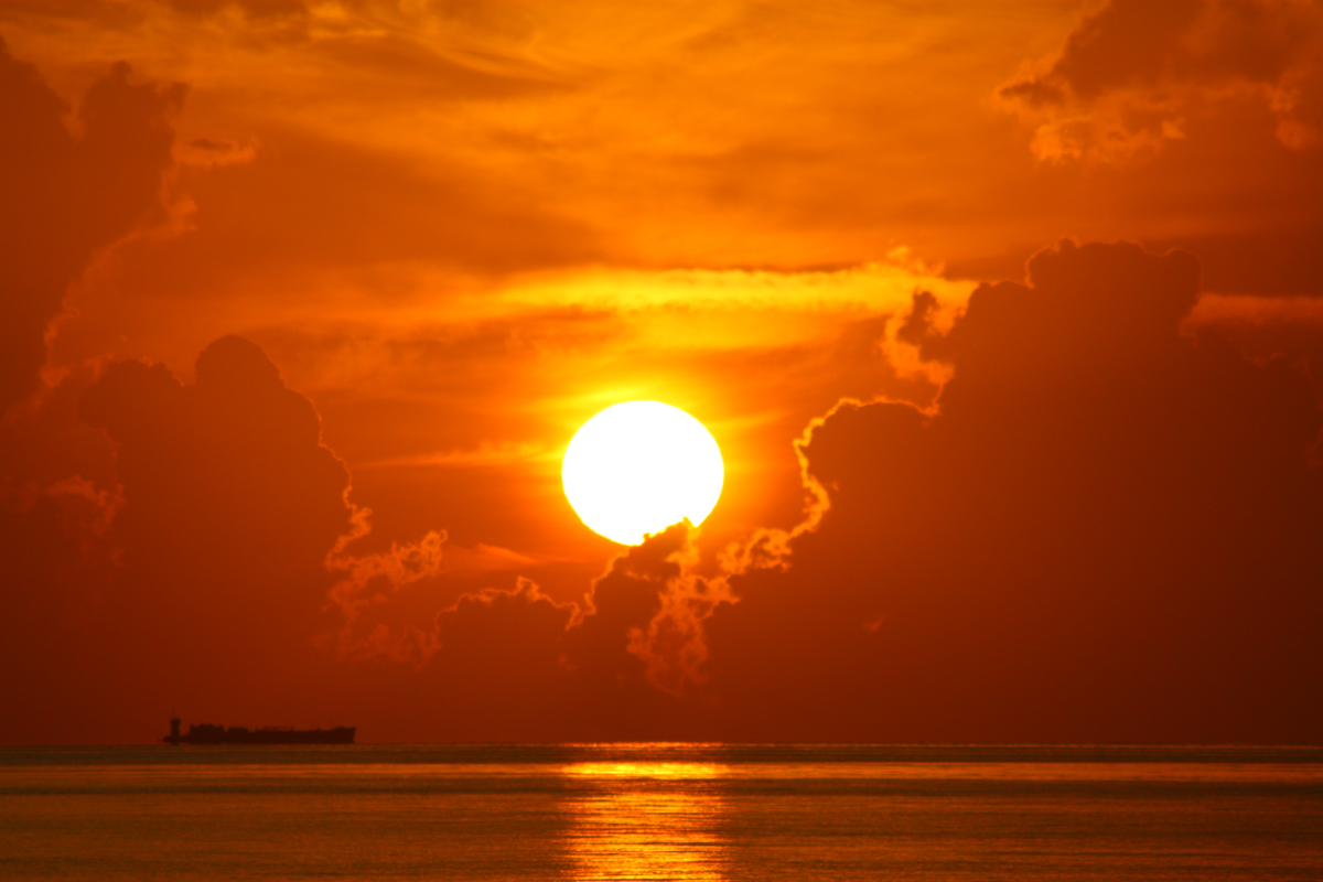 A photo of an orange sun in a sky above the ocean.