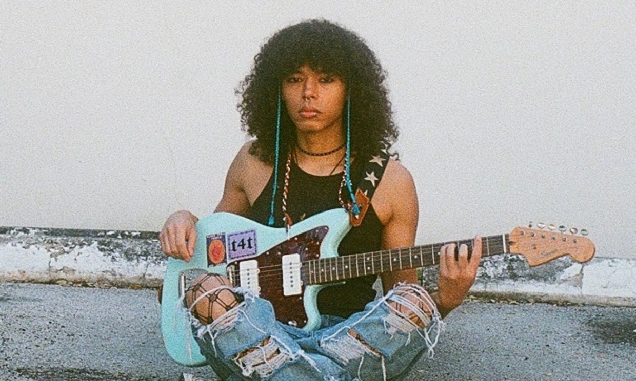 Photo of a young person with curls holding a light blue electric guitar.