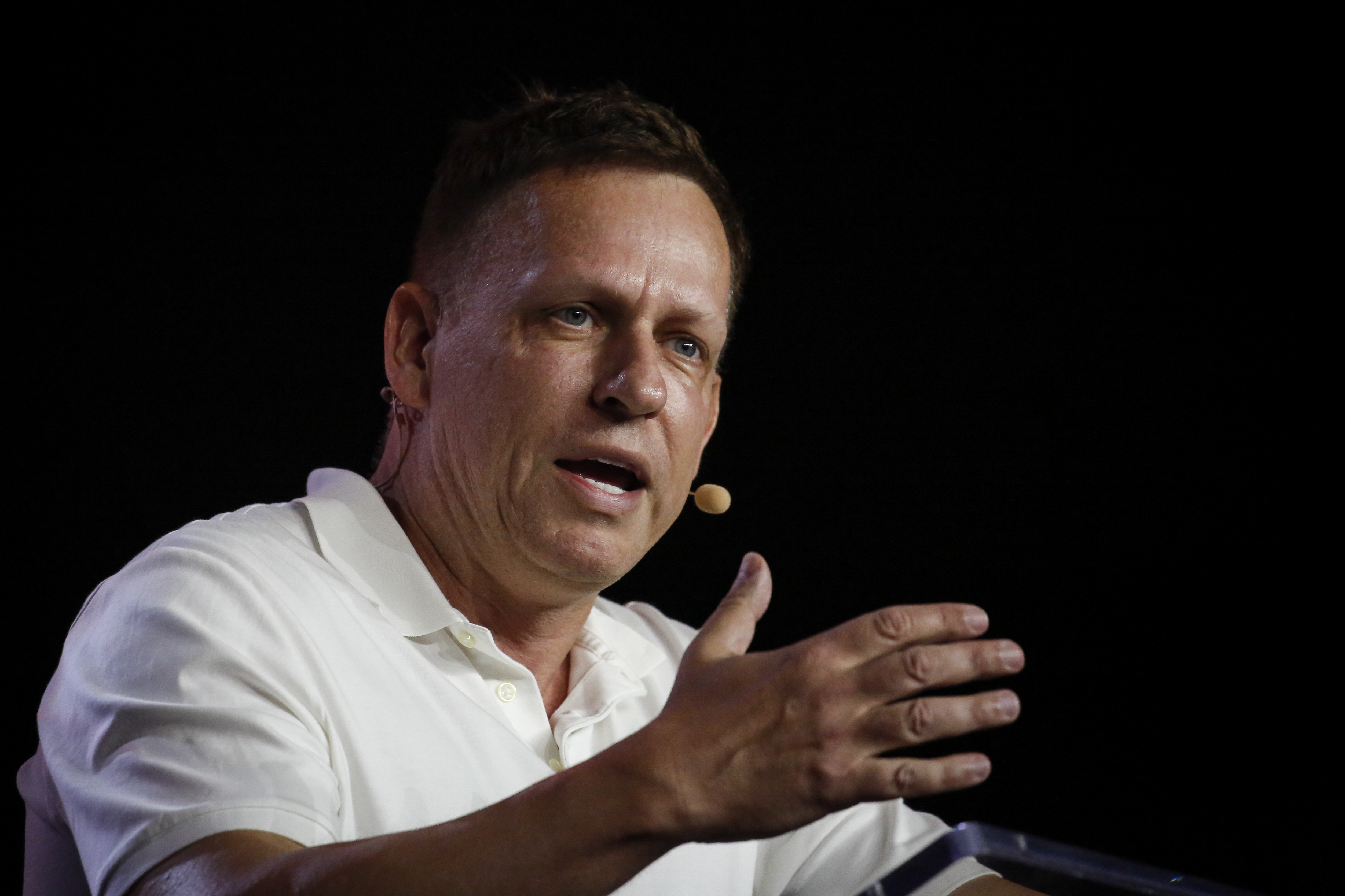 Peter Thiel speaks against a black background while wearing a white collared shirt