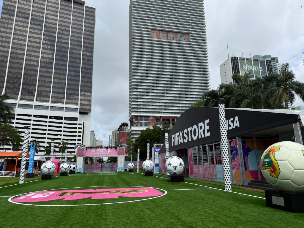 Photo of branded turf with skyscrapers in the background. A tent on right has a sign reading FIFA STORE