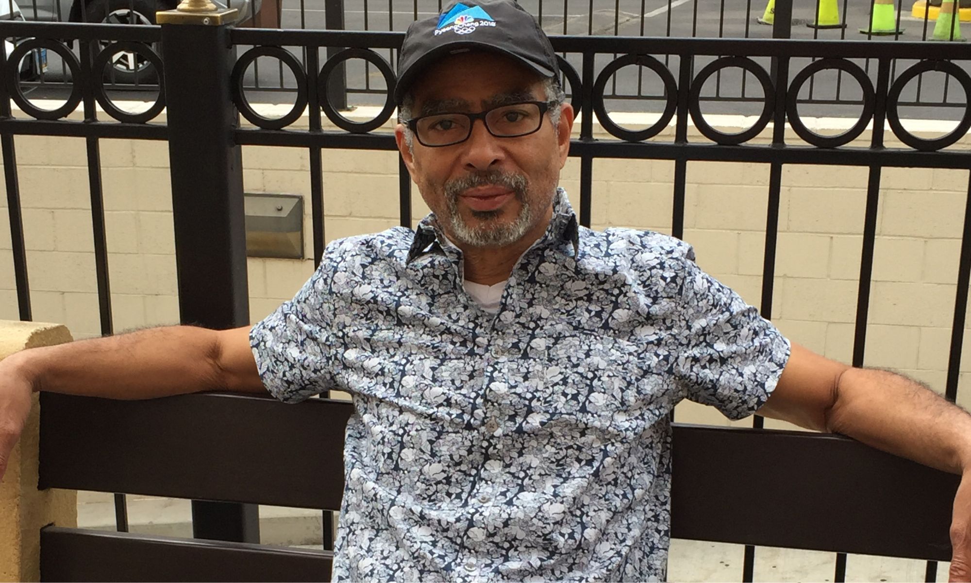 Photo of a man sitting on. a bench wearing a baseball hat.