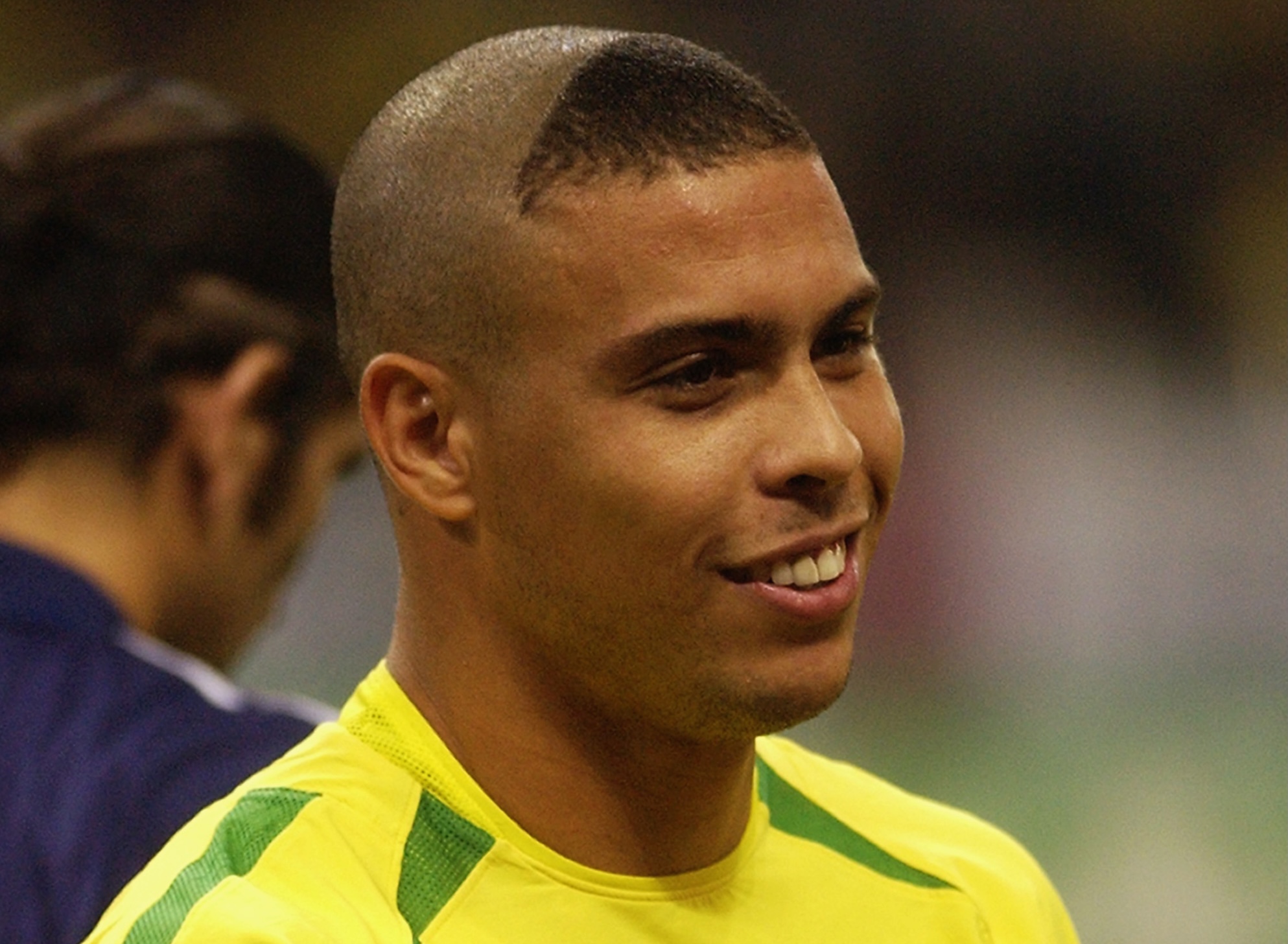 Brazilian soccer player Ronaldo Nazário smiles on the field while sporting a triangle buzz cut