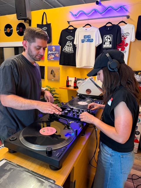 Photo of a man teaching a woman how to DJ on vinyl.