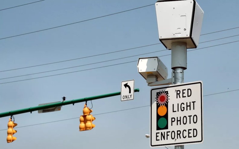 Red light camera with "RED LIGHT PHOTO ENFORCED" sign at intersection