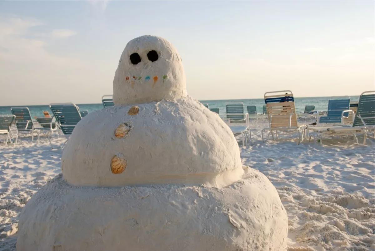 A snowman made of sand sits on a sunny beach.