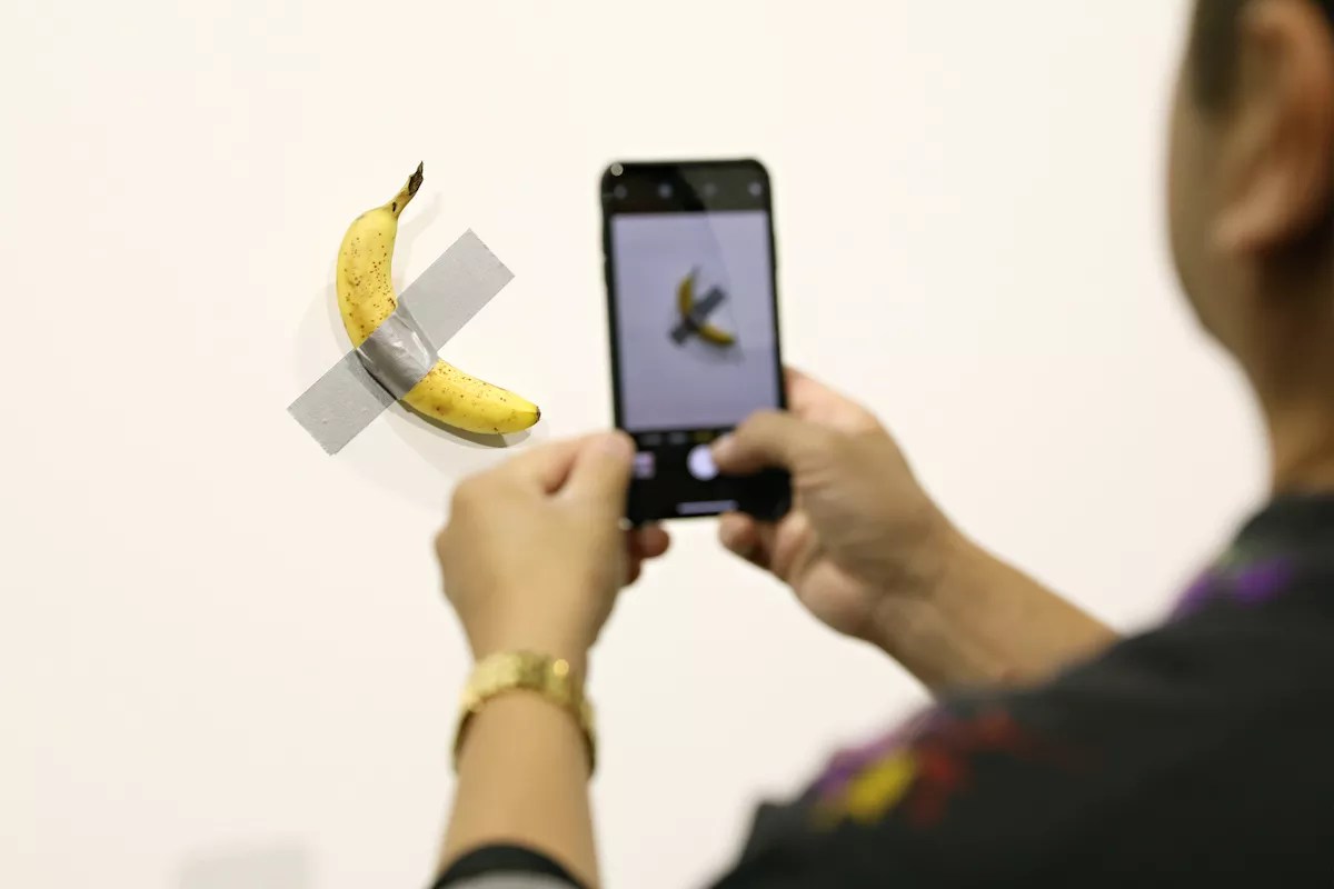 someone taking a picture of a banana duct-taped to a wall