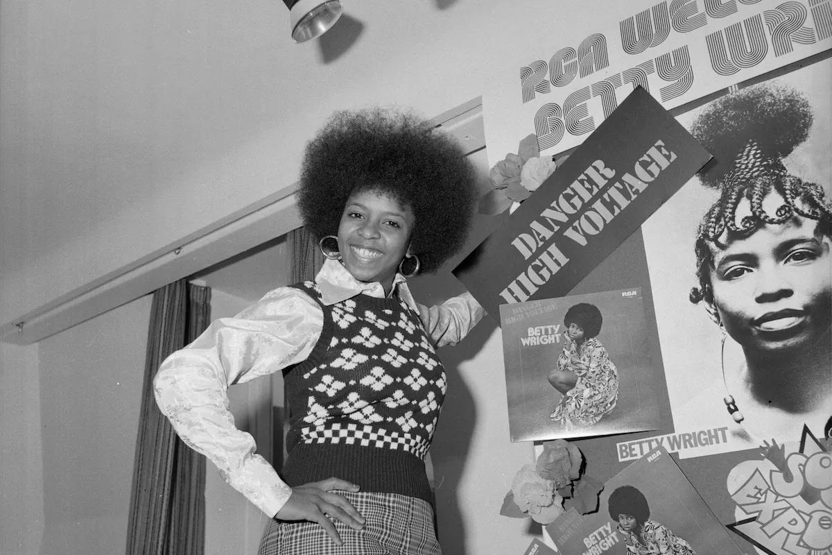 Black and white photo of Betty Wright posing near posters of herself.
