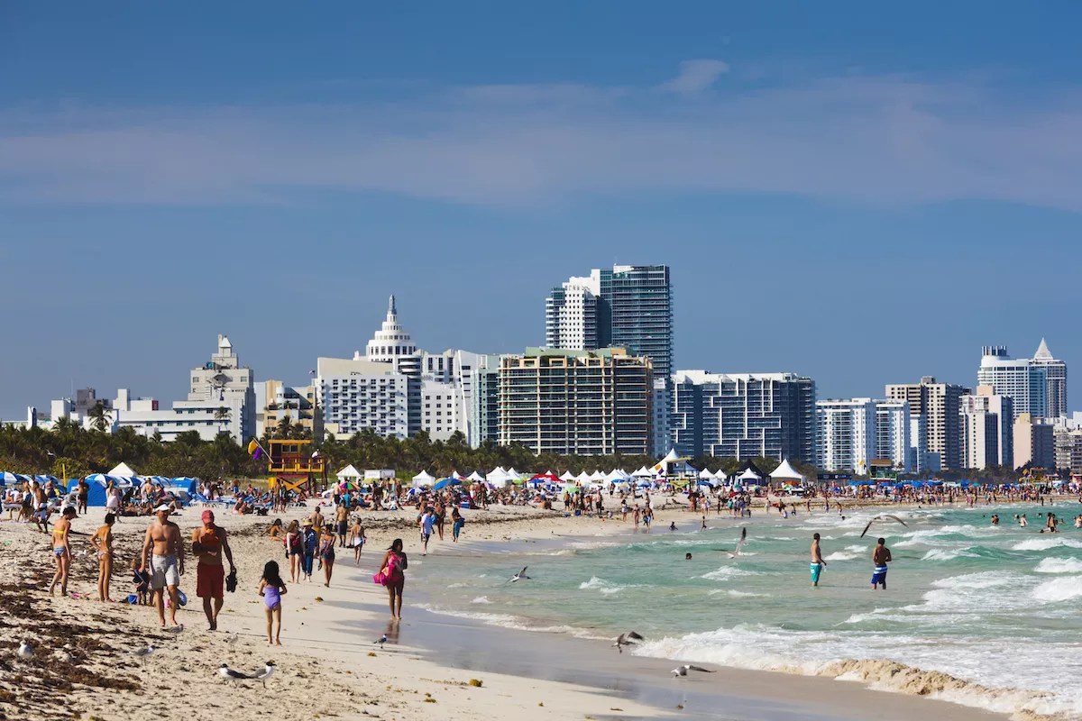 A Miami beach with people walking along it in front of the skyline