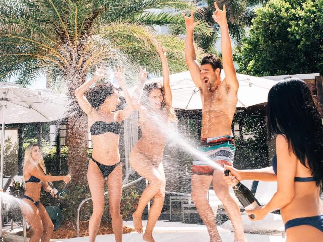 three people dance as someone sprays champagne on them