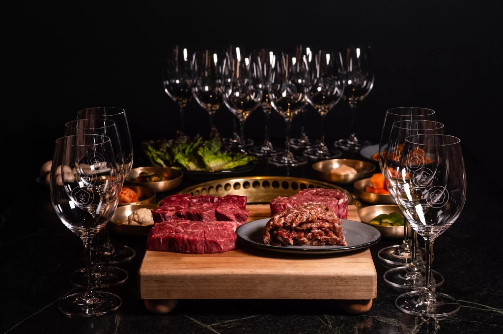 Raw steaks on a cutting board surrounded by empty wine glasses