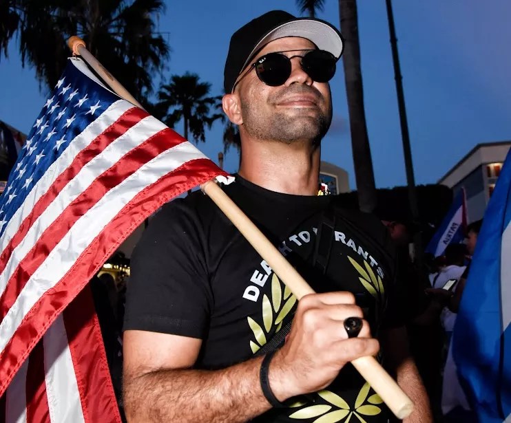 photo of former Proud Boys chairman Enrique "Henry" Tarrio wearing aviator sunglasses and holding an American flag