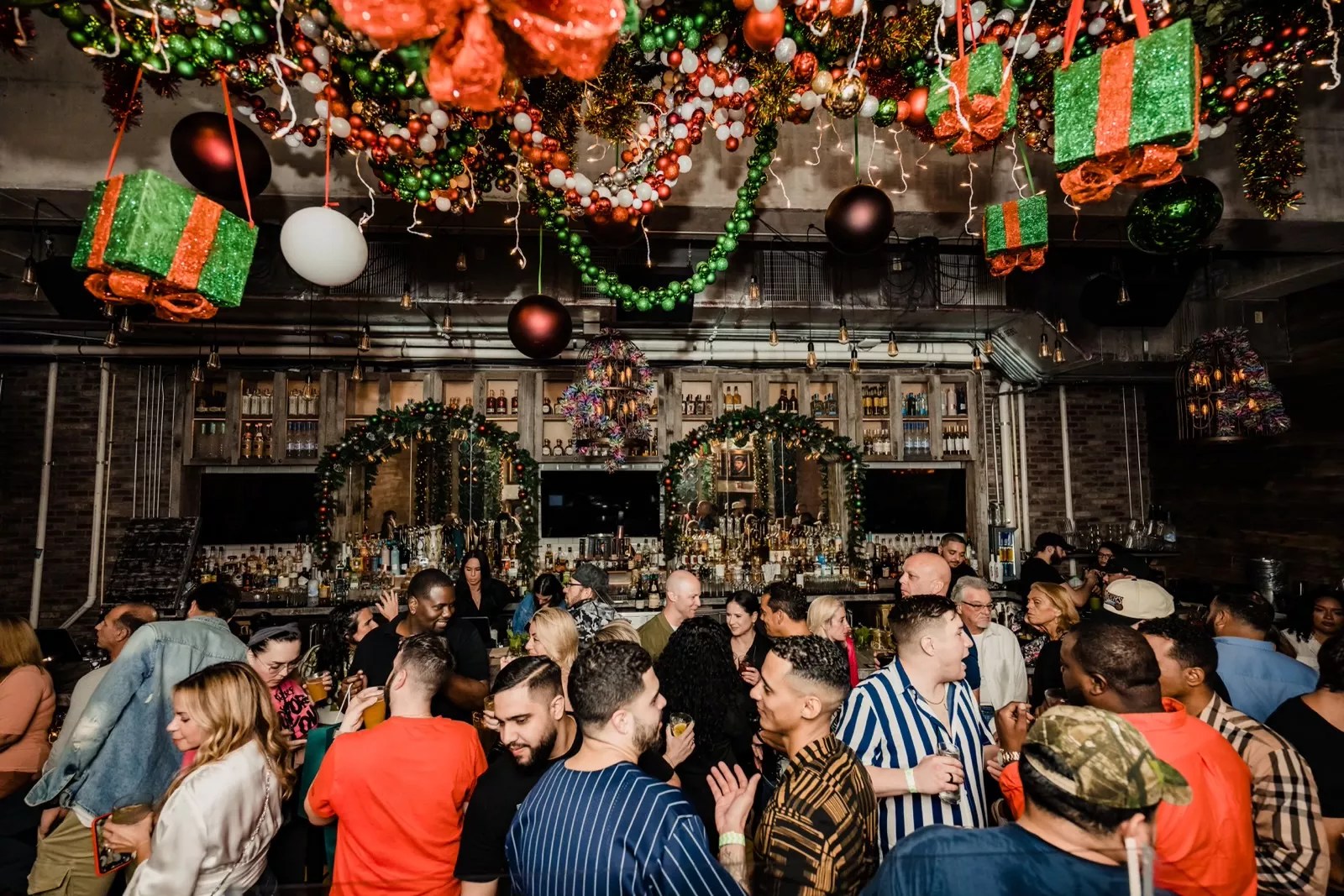 Guests mingle with cheer as they're surrounded by fun holiday decorations at Bodega Taqueria y Tequila. The ceiling is draped in holiday decoras guests hold and sip colorful holiday cocktails.