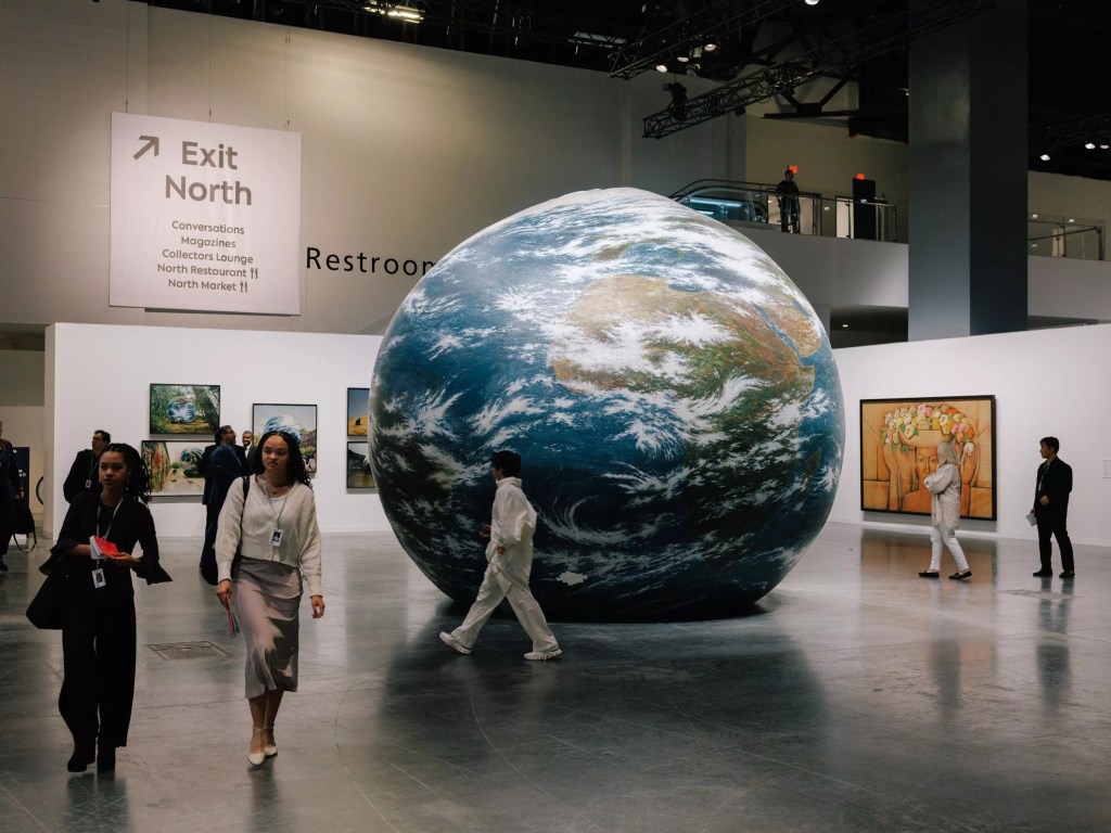 photo of people walking around a gallery with a massive globe sculpture in the center