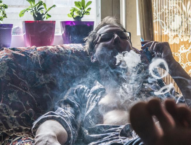 A man blows smoke rings from a hookah on his couch