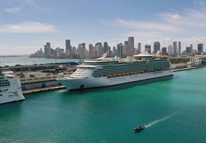 A large cruise ship docked in a port, with the Miami skyline in the background.