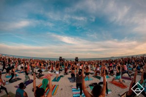 A large group of people doing yoga on the beach at dawn