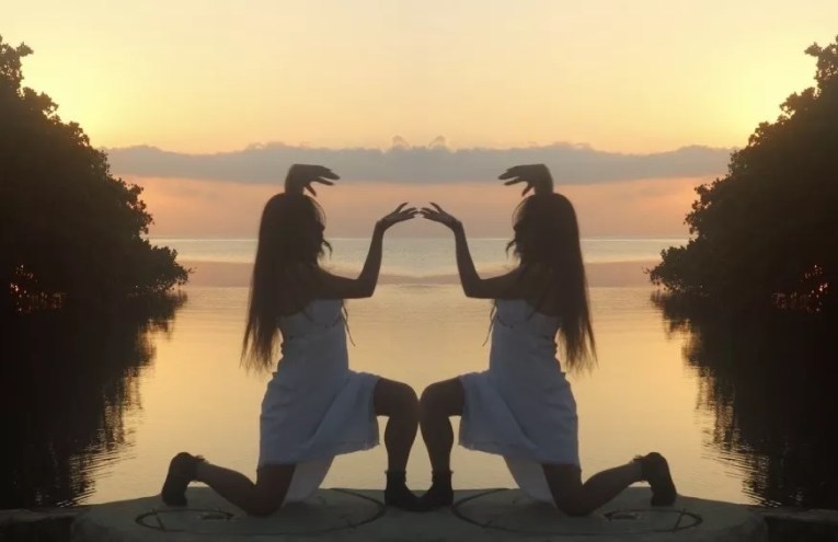 Still image from Caracoles en Cemento of a woman mirrored as she kneels with a sunset behind her