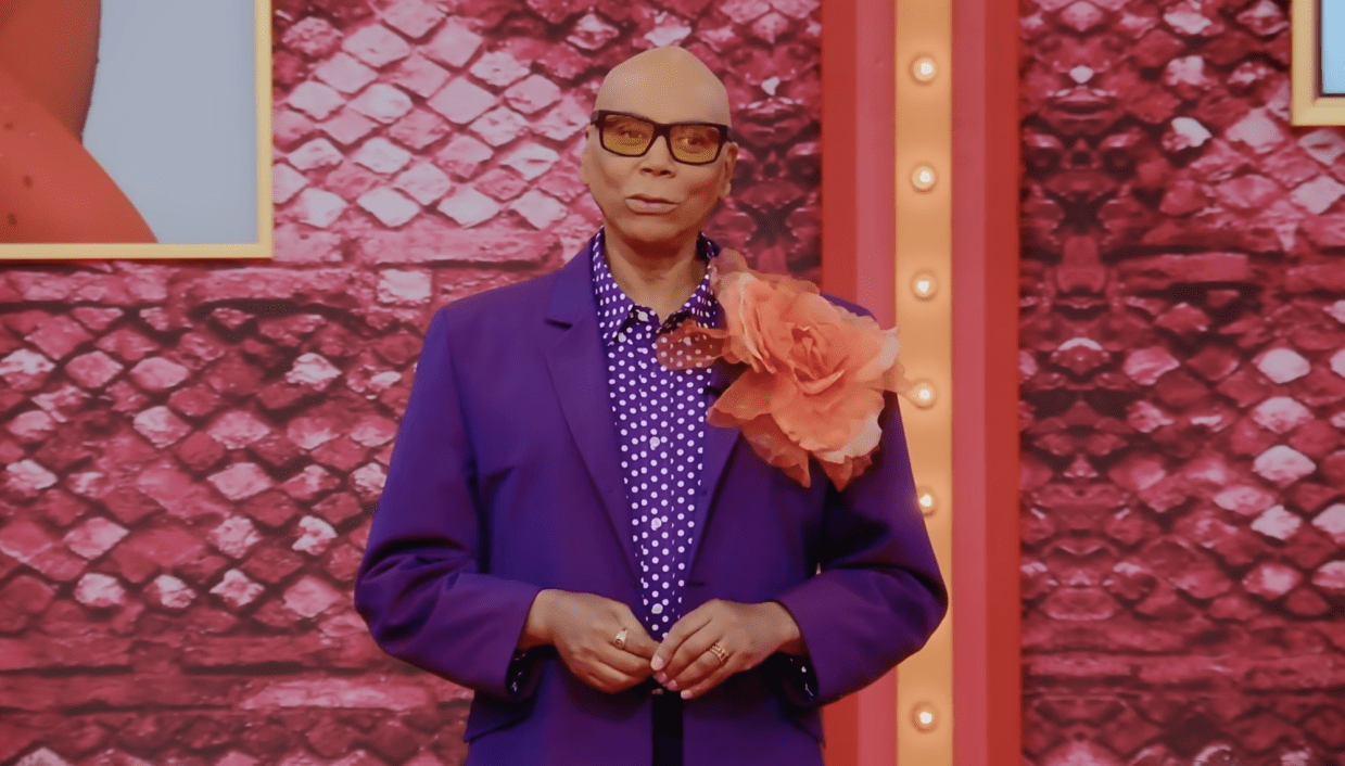 RuPaul standing in the Werk Room in a purple suit