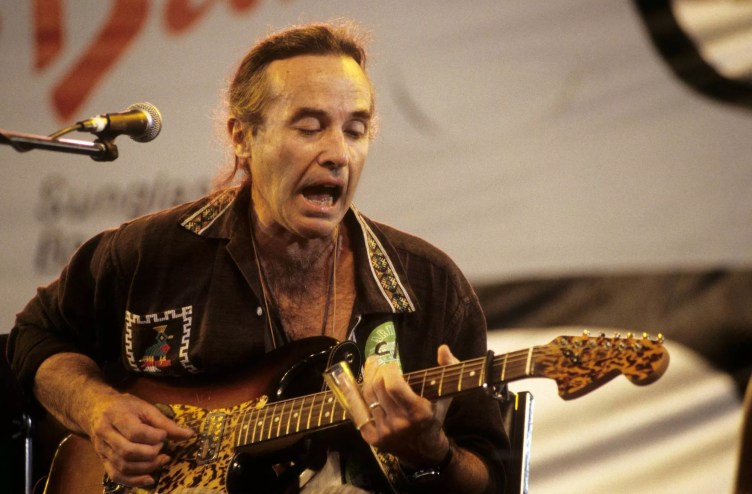 Ry Cooder performing on stage with a guitar in hand