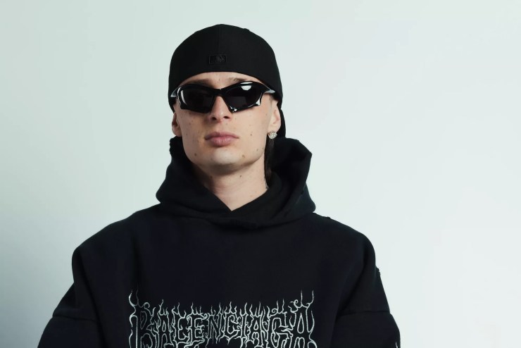 Peso Pluma wearing sunglasses and a black Balenciaga hoodie