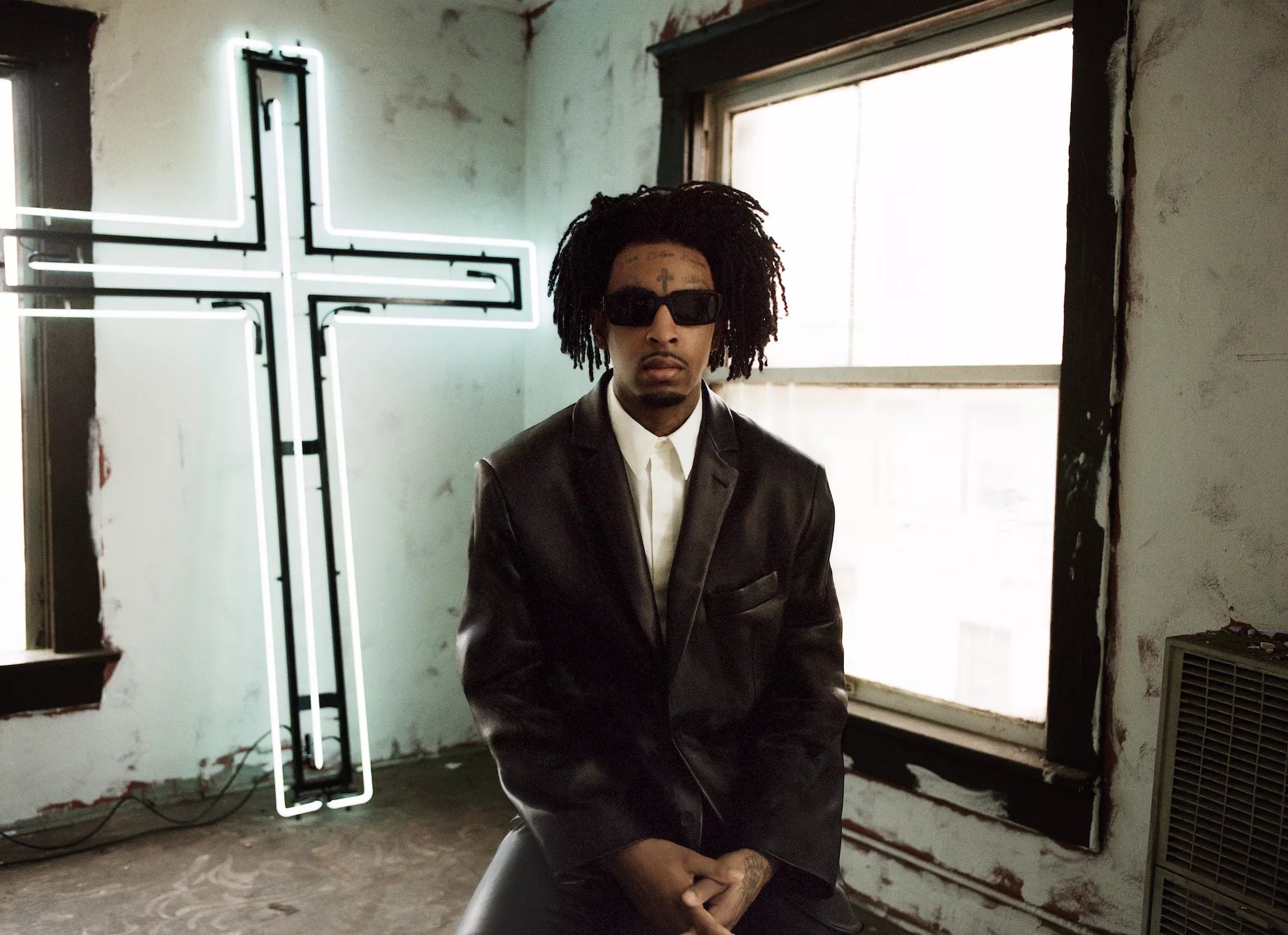 21 Savage sitting down with a cross behind him
