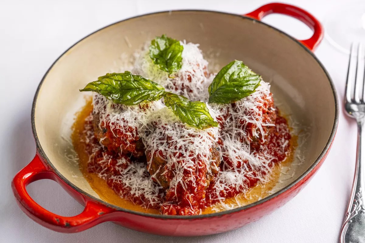 Meatballs topped with basil and finely shredded cheese in a red enameled iron pot