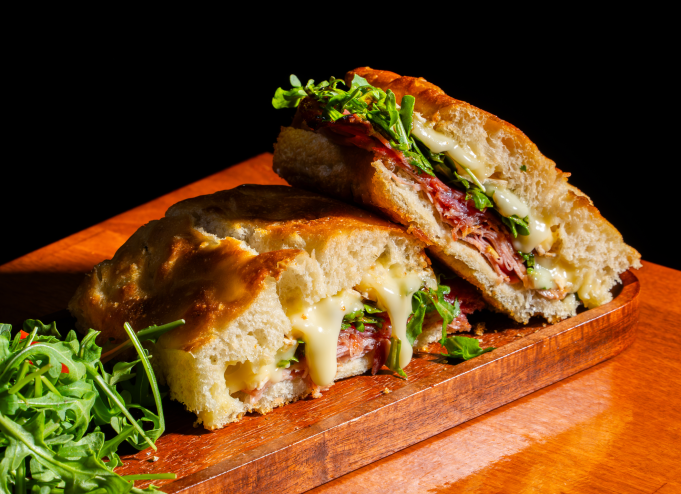 An Italian sandwich with cheese and arugula on a wooden platter