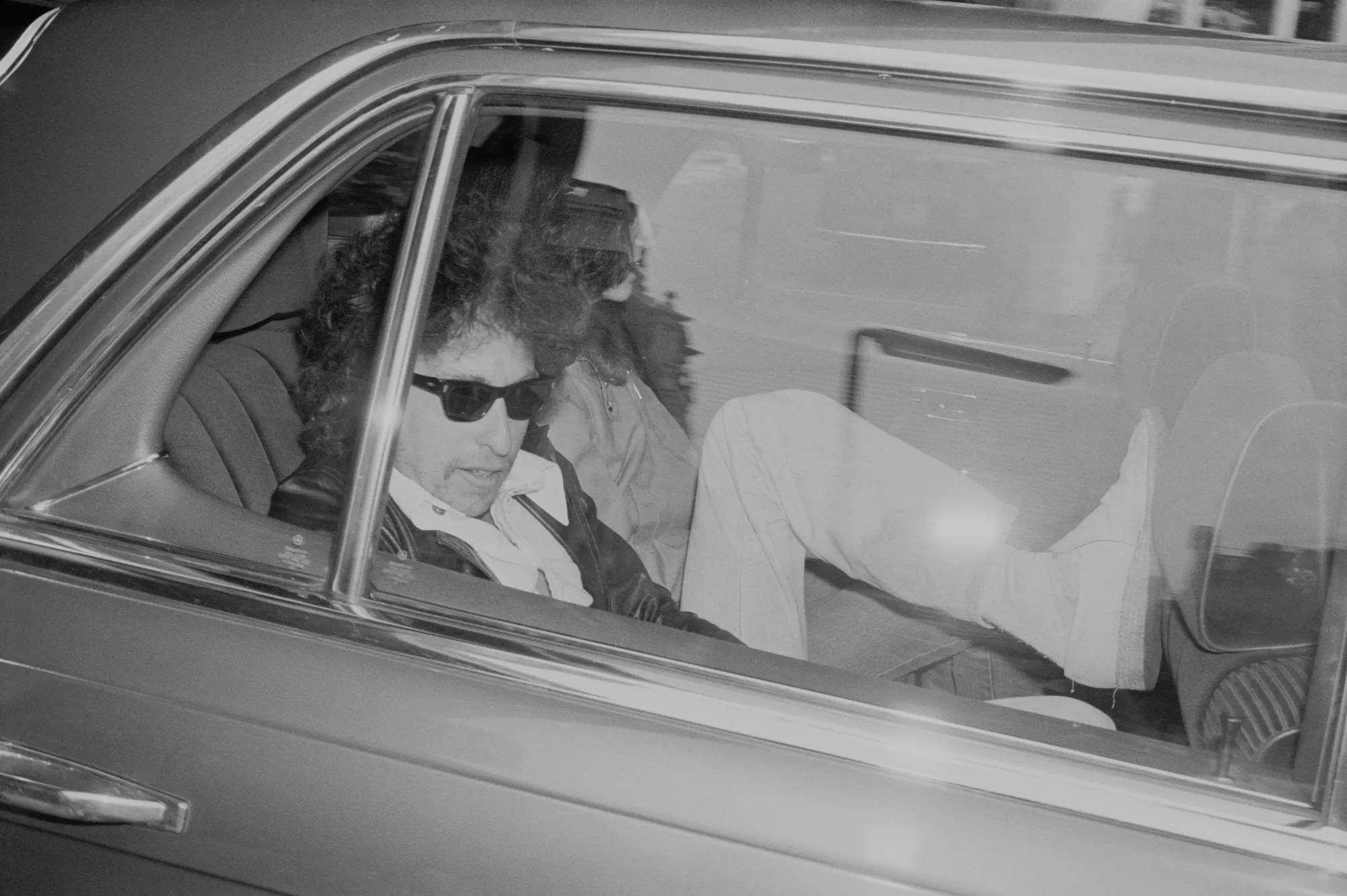 Black and white image of Bob Dylan in the back of car