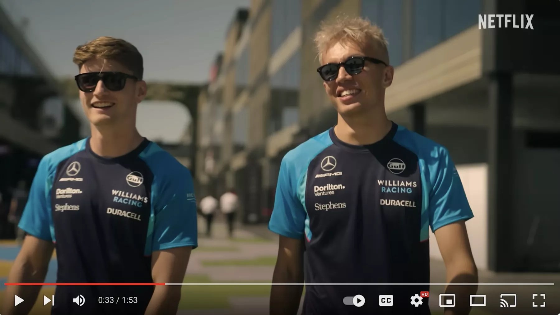 Williams Racing Formula 1 drivers Logan Sargeant (left) and Alex Albon (right) walk alongside each other wearing sunglasses.