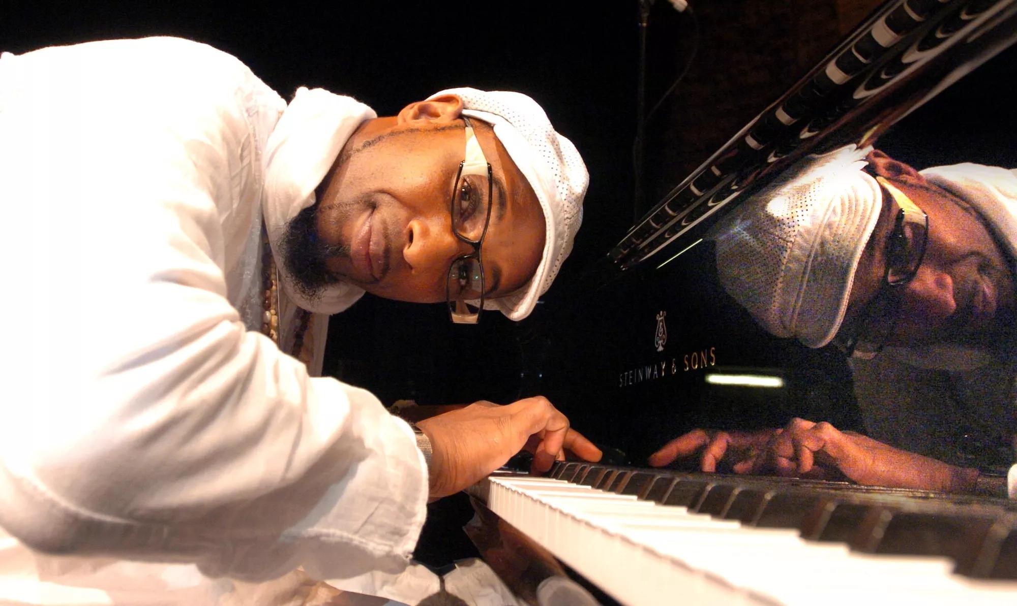 Omar Sosa leaning over the keys of his piano while looking at the camera