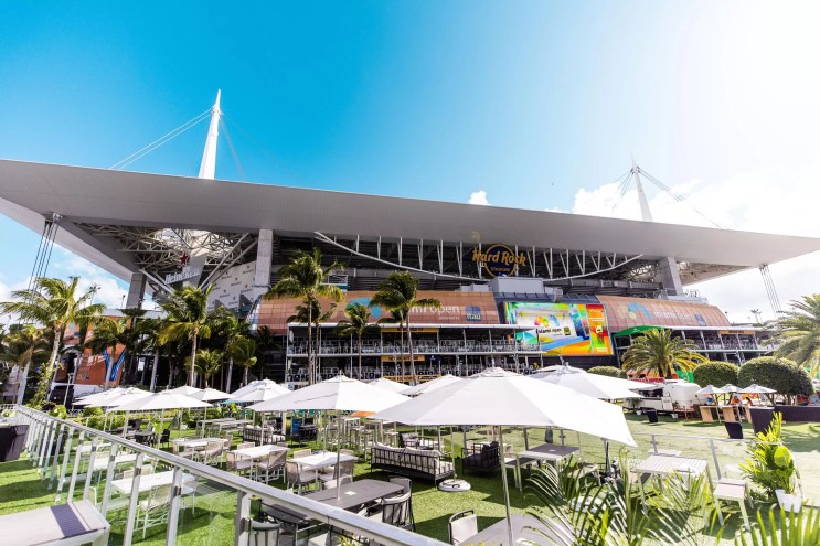 The sun shines on Hard Rock Stadium, a rectangular windowed building with a flat, wide roof