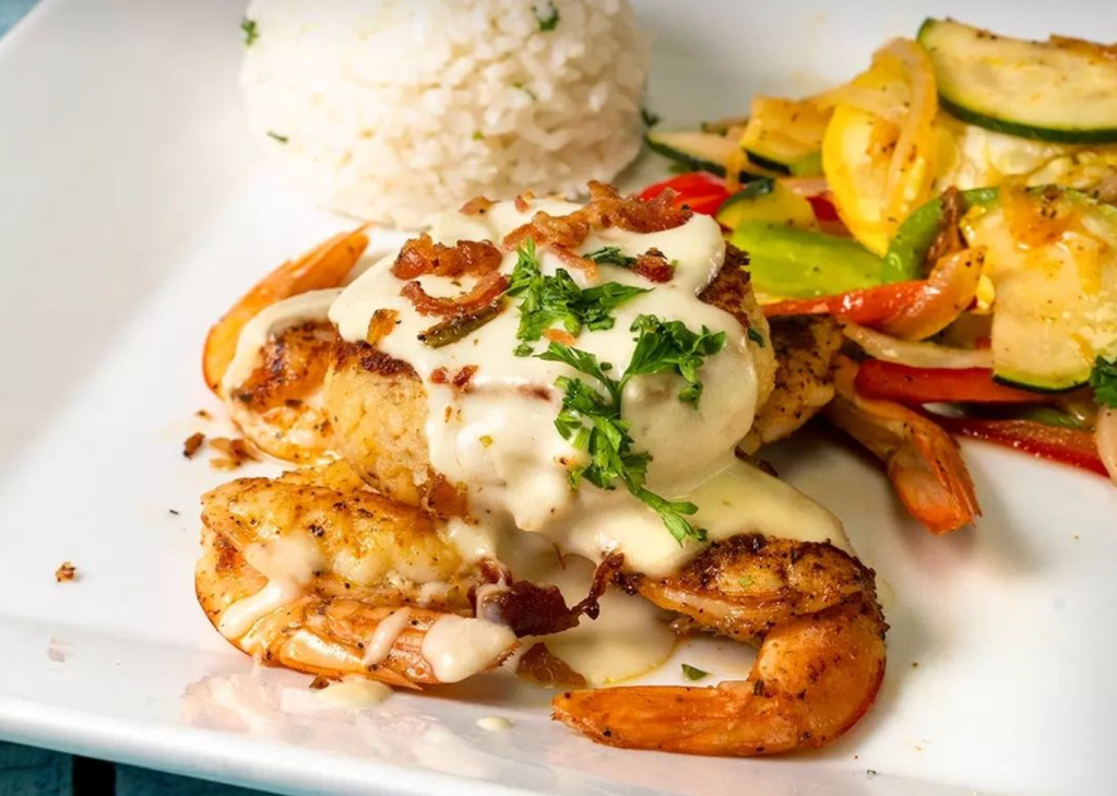 A plate of seafood, rice, and vegetables with a creamy sauce