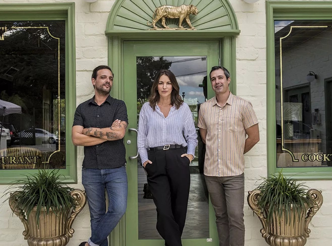 Three people outside of a light green building and light green door