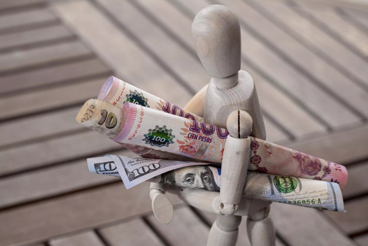 A stock photo of a faceless figurine carrying Argentinian pesos and U.S. dollars
