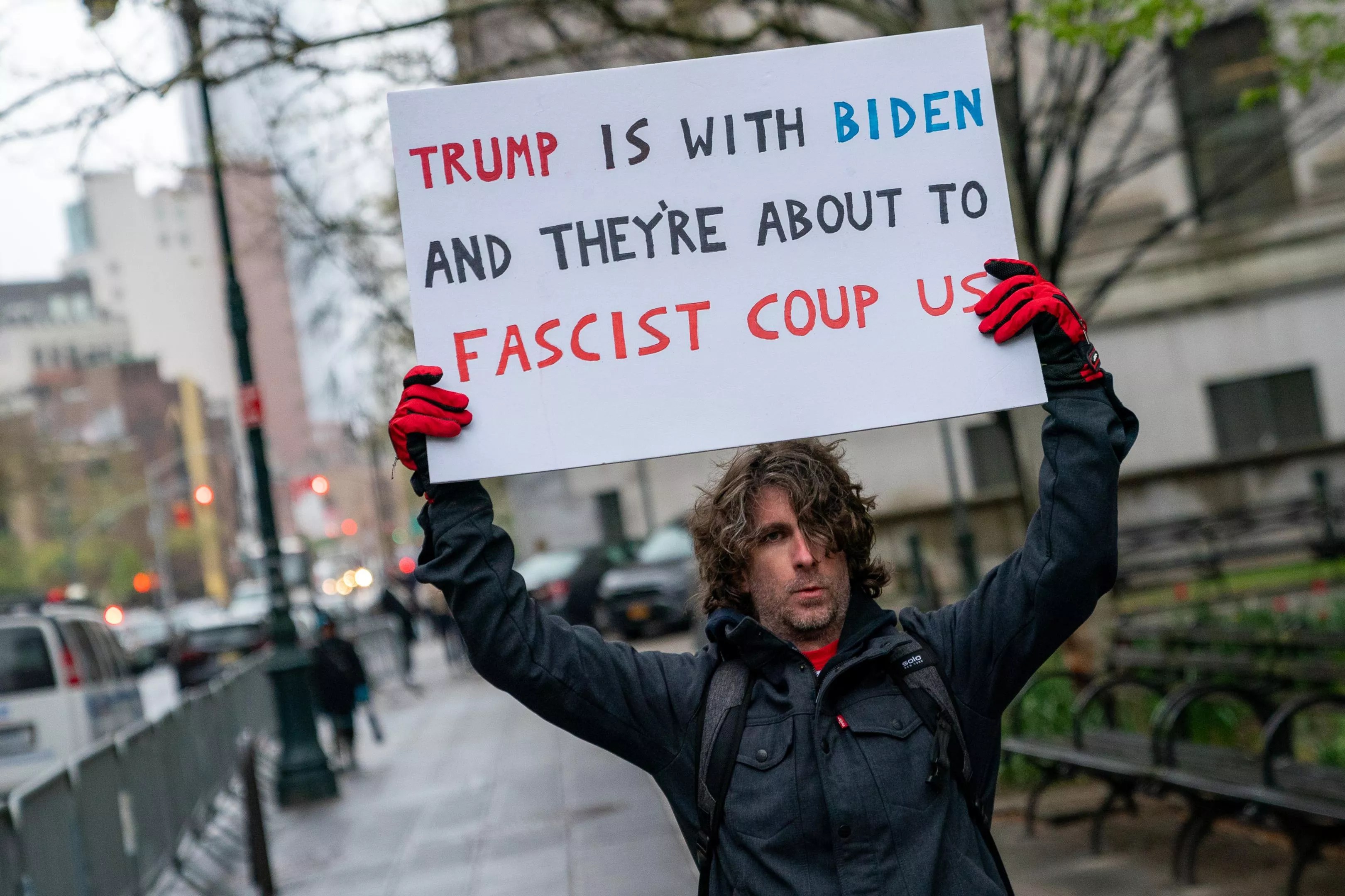 Max Azzarello holds up a sign that reads, "Trump is with Biden, and they're about to fascist coup us."