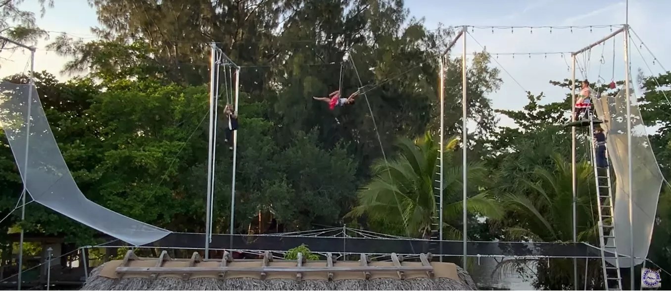 A trapeze artist swings in the air in a modular trapeze rig set up in a Miami man's backyard