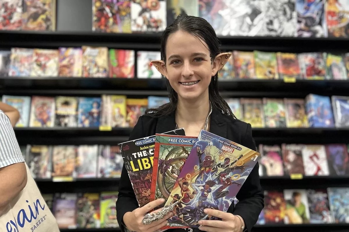A woman with prosthetic ears holding comic books in her hands