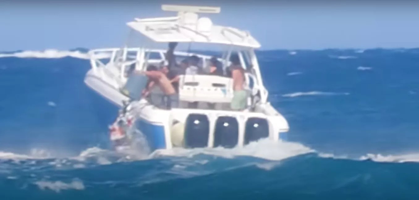 A boat full of teenagers navigates rough waters as one boy dumps a trash can full of garbage into the ocean