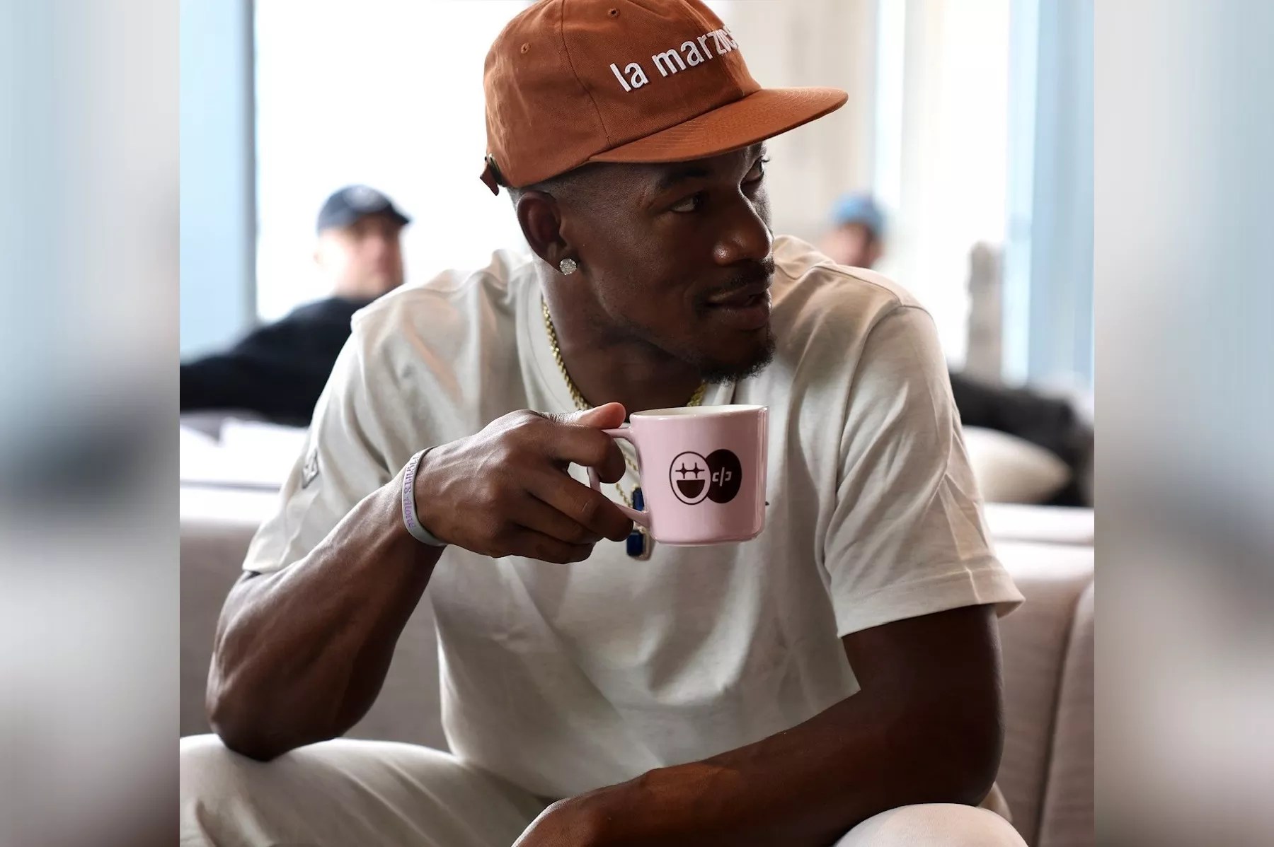 Basketball star Jimmy Butler wearing a ballcap and drinking coffee out of a Bigface branded mug