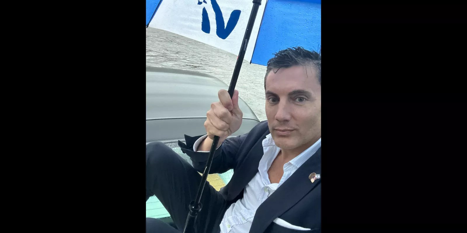 Fabián Basabe sitting on top of his car in a flood, with an umbrella