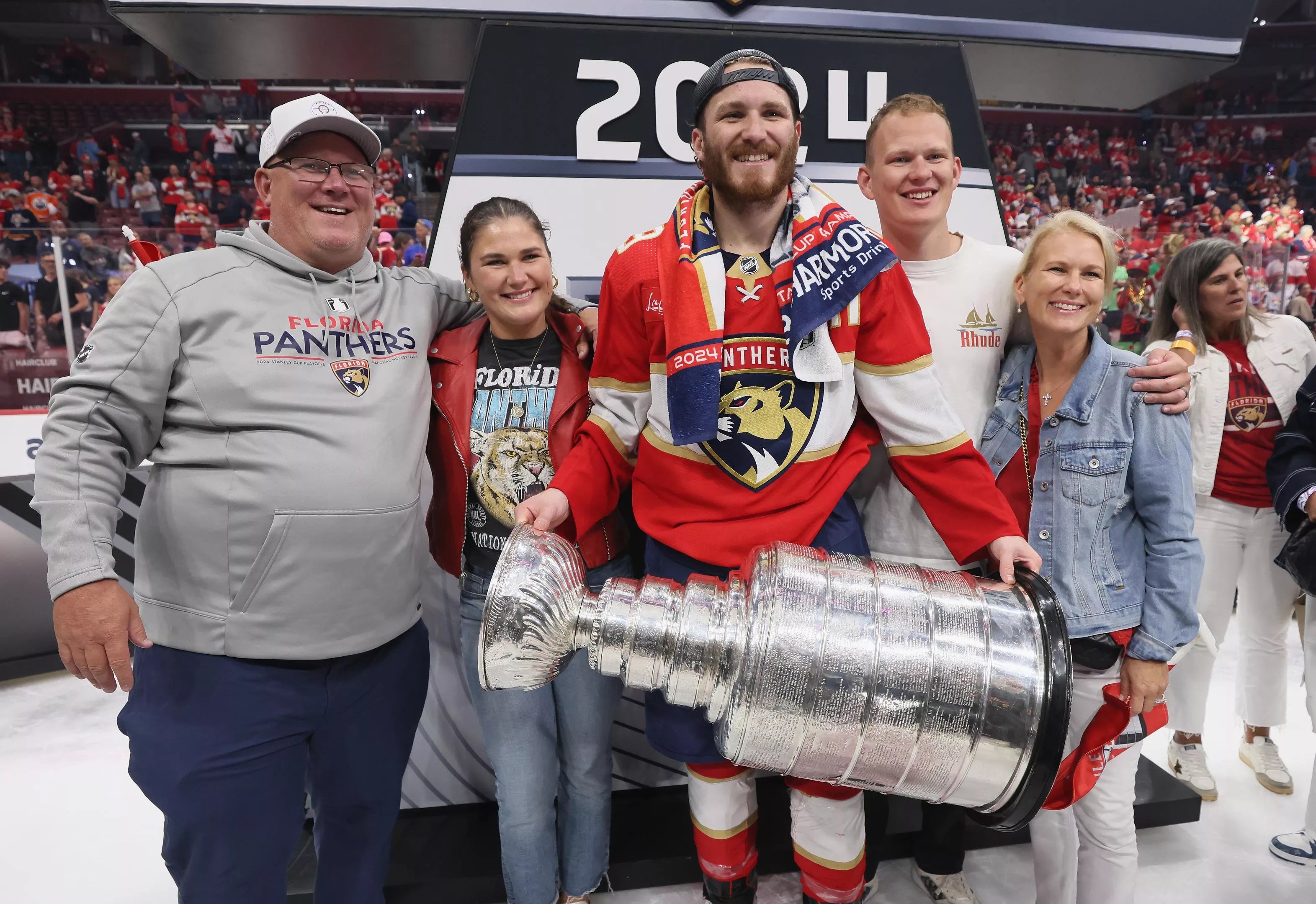 Panthers player Matthew Tkachuk holds the Stanley Cup trophy as his family stands shoulder to shoulder next to him, smiling