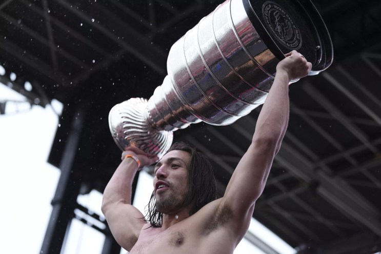A soggy, shirtless hockey player named Ryan Lomberg hoists the Stanley Cup trophy over his head