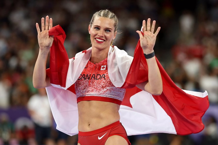 Pole vaulting champion Alysha Newman, wearing cornrolls in her hair and draped in the Canadian flag, waves during the Paris Olympics