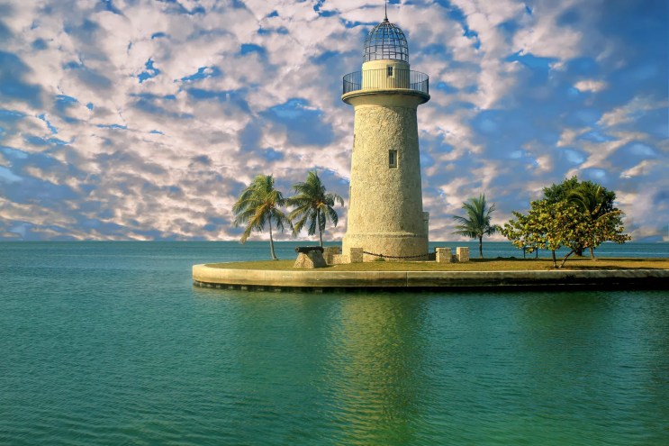 Patches of clouds white clouds on a bright blue sky behind a stout limestone lighthouse