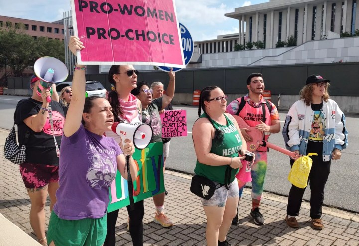 photo of a group outside the Florida Supreme Court, holding megaphones and pink signs with slogans such as "Pro-Women Pro-Choice"