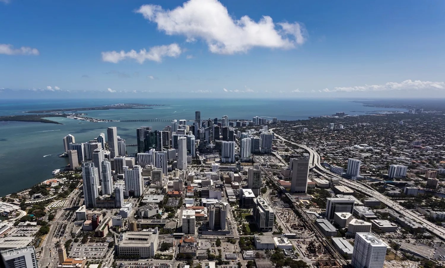 color aerial shot from high over downtown Miami with view of ocean, buildings, and streets on a beautiful sunny day