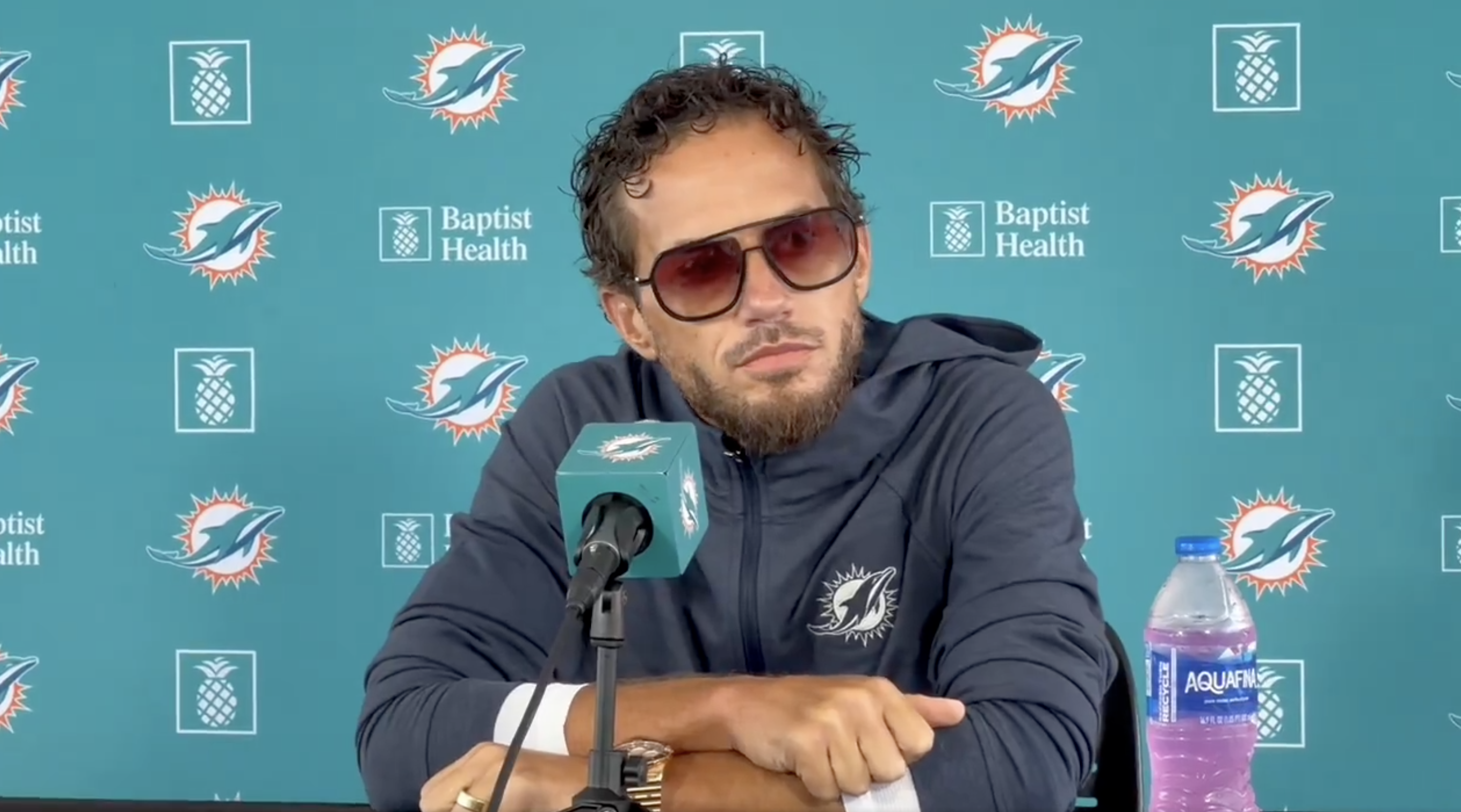 Mike McDaniel speaks at press conference with flashy shades, curly hair, and an overgrown beard.