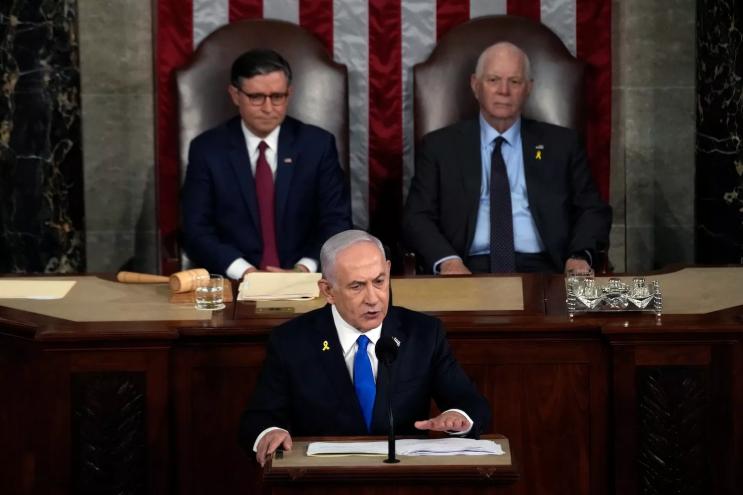 netanyahu at the dais with Speaker of the House Mike Johnson (R-LA) and U.S. Sen. Ben Cardin (D-MD) seated in the background, flanking him and slightly out of focus