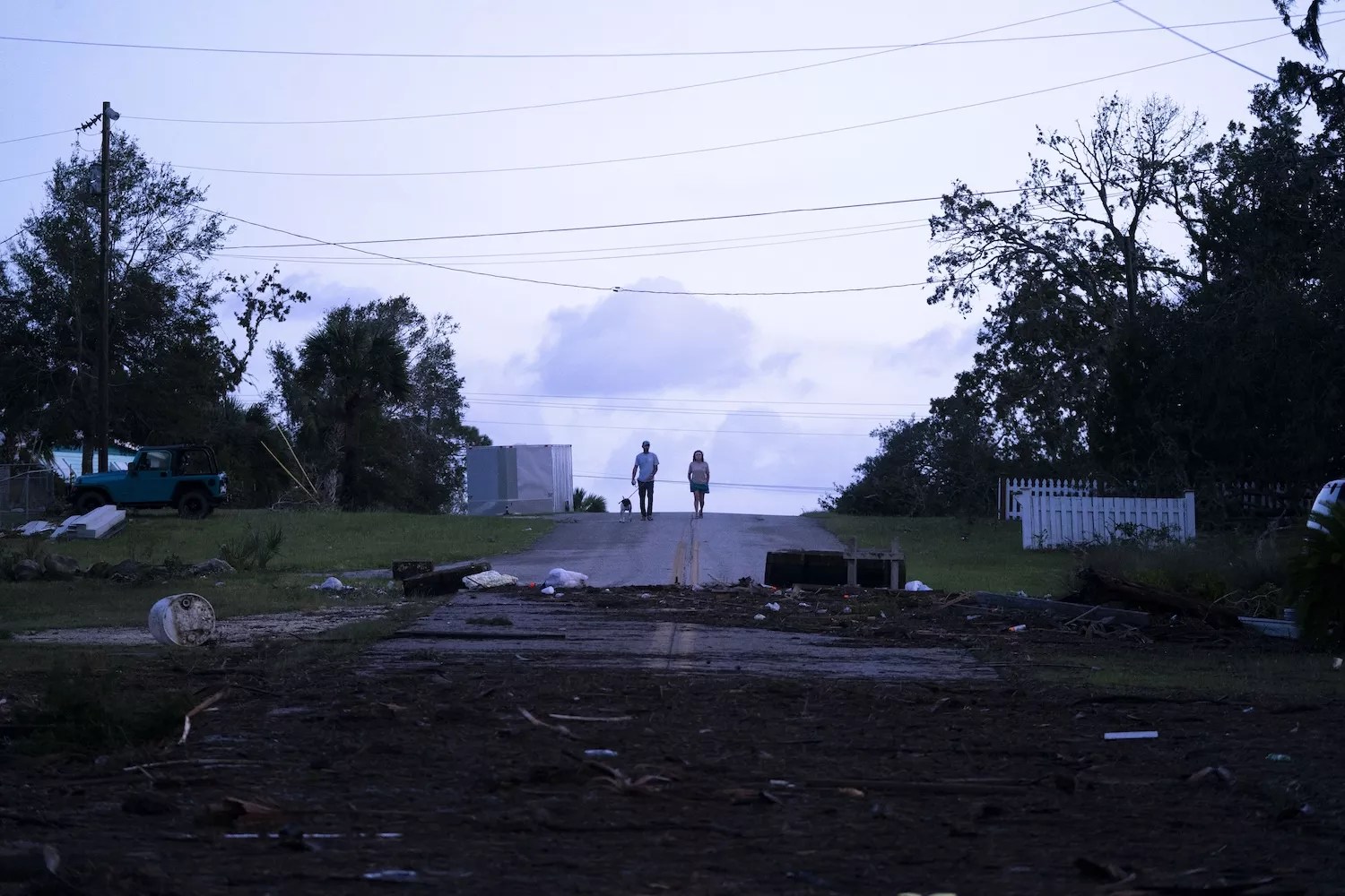 People walk down a street with a dog in the aftermath of Hurricane Helene on September 27, 2024, near Steinhatchee, Florida. Hurricane Helene made landfall nearby the previous night as a category four storm but has weakened as it moves inland.