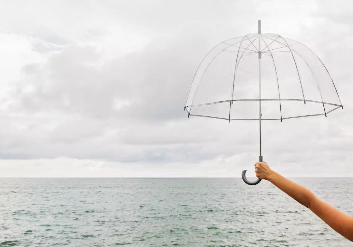 Person holding umbrella against cloudy sky over ocean